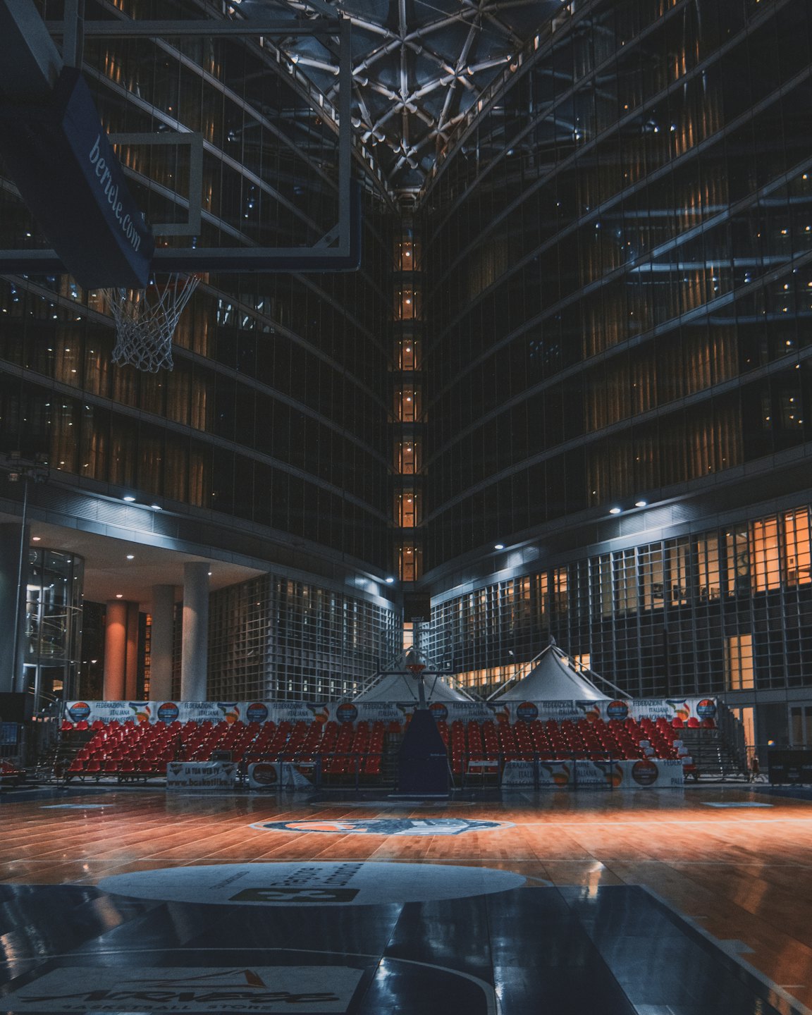Empty indoor basketball court surrounded by rows of spectator seats.