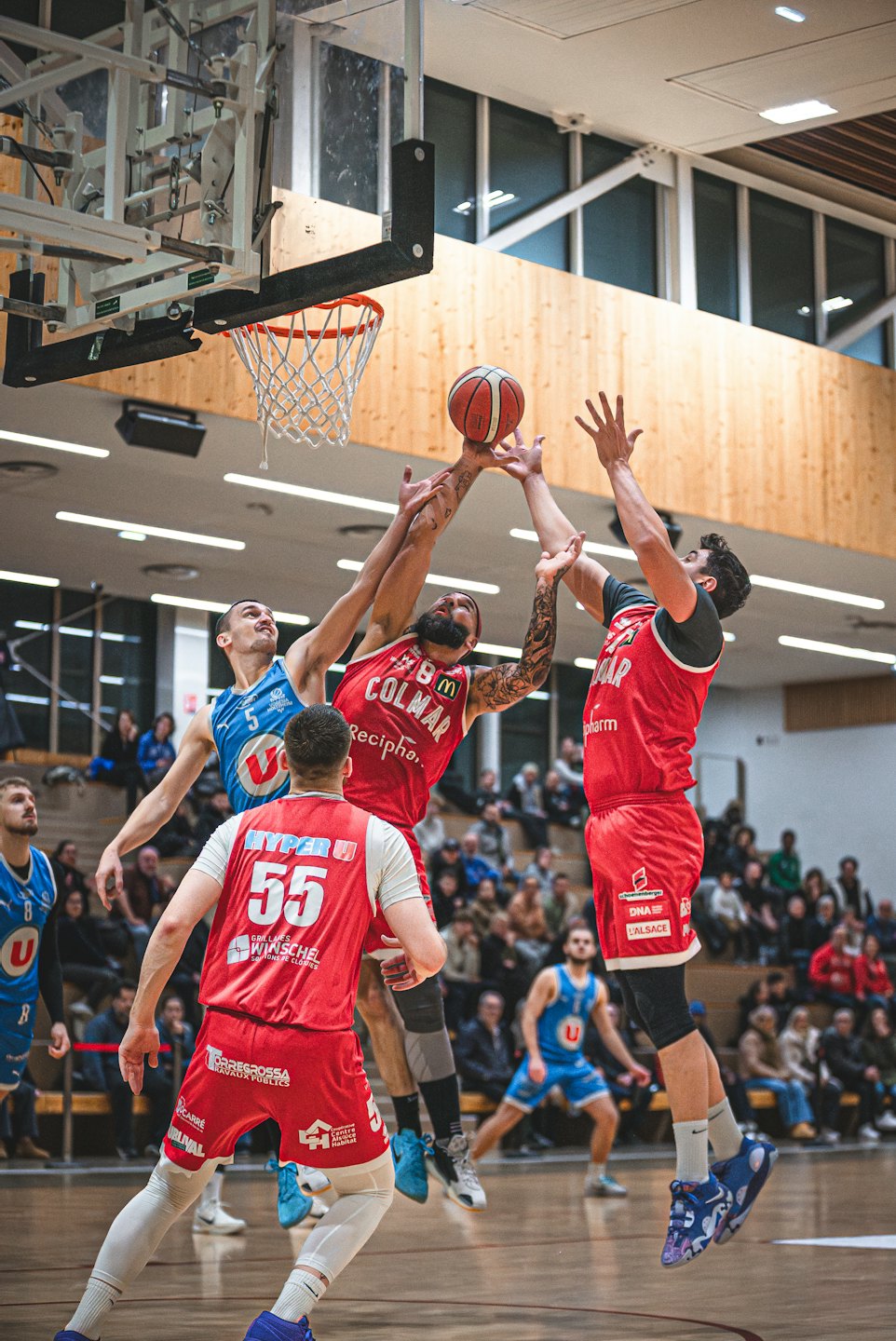 Basketball players jumping to reach the ball near the hoop.