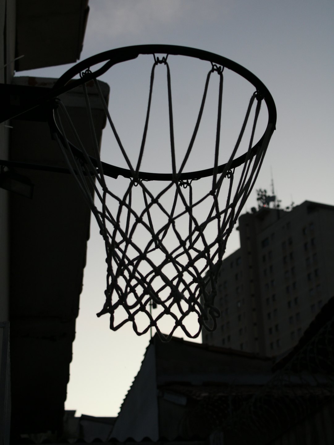 A basketball hoop stands against an overcast urban skyline.