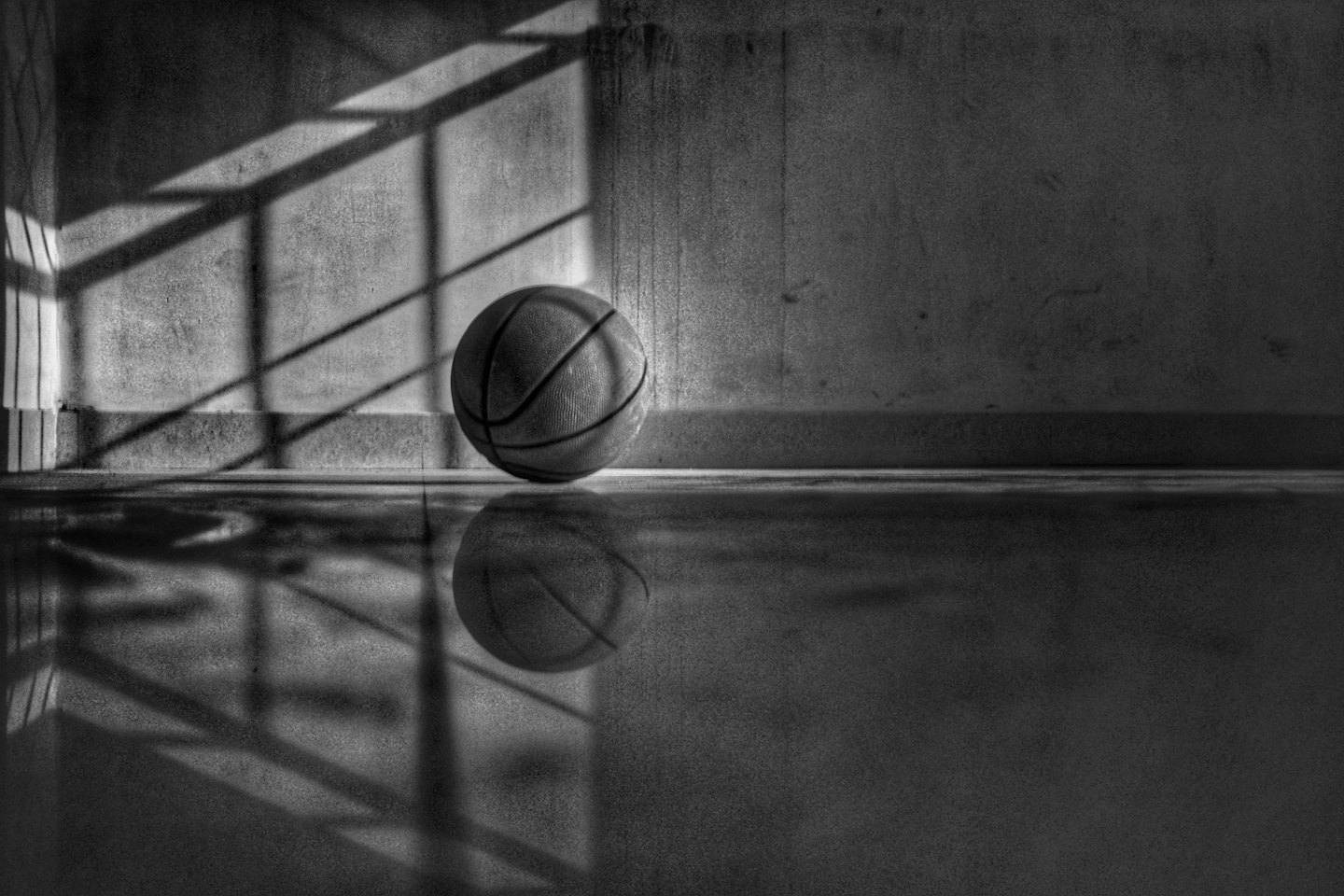 A basketball sits on a shiny floor in front of a concrete wall.