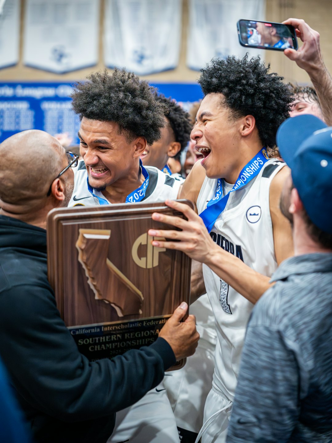 Two basketball players celebrate winning a championship with a trophy.