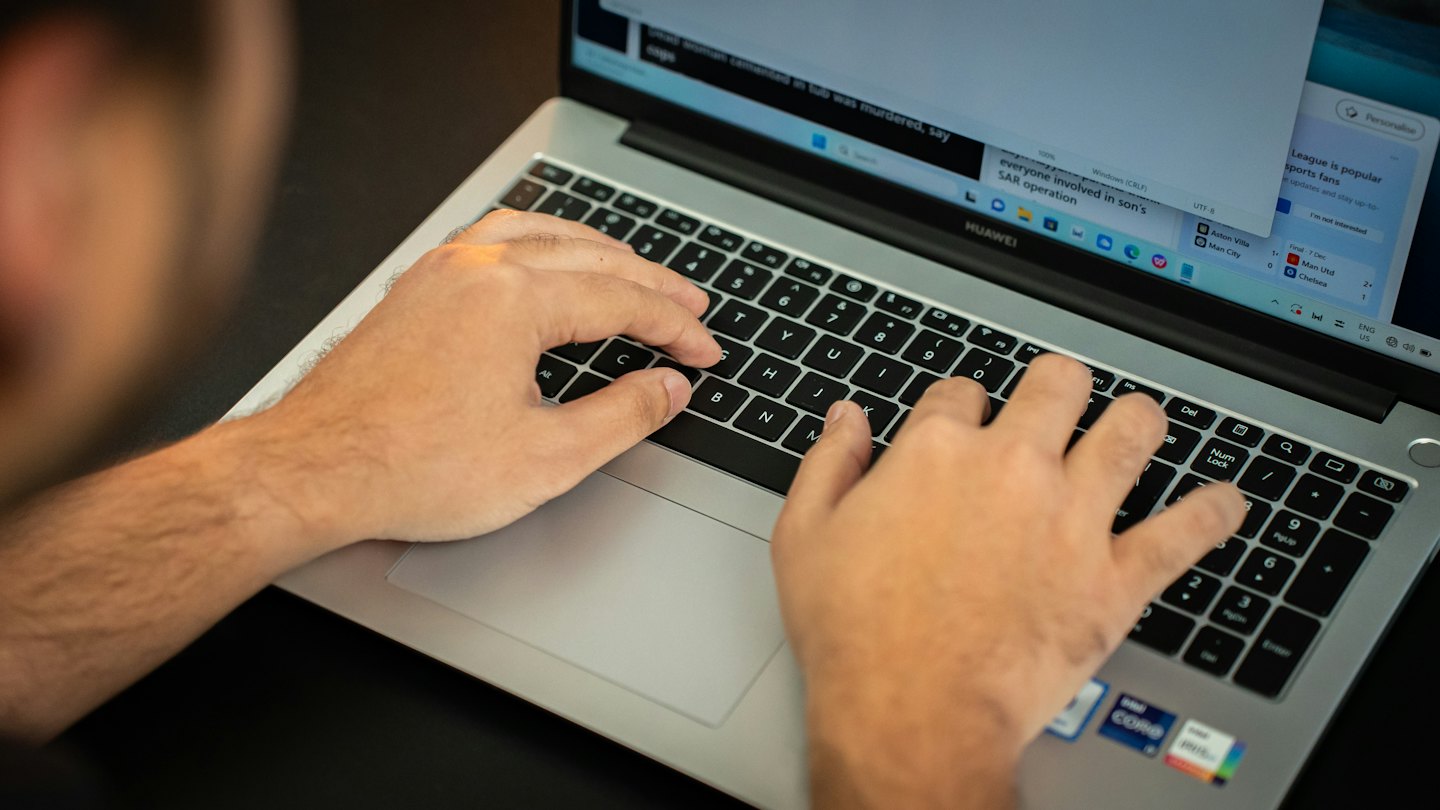 A person types on a laptop displaying information and headlines.